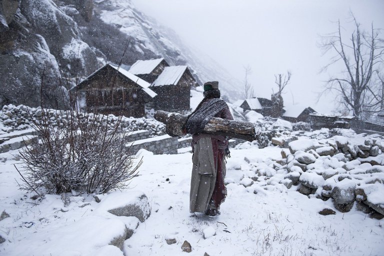 People Third Place Photo and caption by Mattia Passarini / National Geographic Travel Photographer of the Year Contest Remote life at -21 degree Kinnaura tribal old women in remote village in Himachal Pradesh carrying big log back home to warm up her house